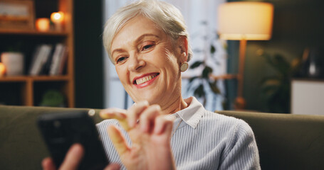 Poster - Online, smile and mature woman with cellphone, reading and information in news and home in night. Living room, relax and person on couch with mobile, contemplating or wonder with subscription to app