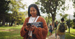 © peopleimages.com - Student, woman and books in park with phone on walk with education, learning or thinking for development at campus. Person, reading and app on path, social media and scholarship at college in Brazil