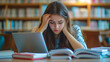 © aun - A young woman studying at home with her laptop and books spread out on the table
