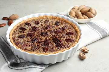 Wall Mural - Delicious pecan pie in baking dish and fresh nuts on gray textured table, closeup