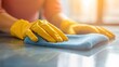 © Dusit - Close up of a woman's hand in yellow gloves cleaning a table with a blue microfiber cloth..