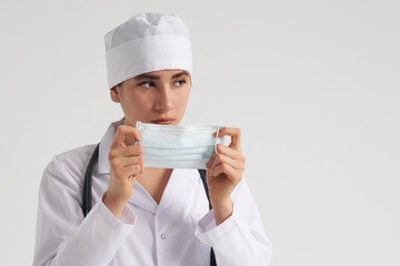 Portrait of young female doctor putting on protective medical face mask on white background