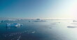 © mozgova - Sunny Antarctica ocean aerial landscape. Icebergs and ice floes floating polar water under bright blue sun sky. Global warming, climate change, melting ice. Panoramic drone flight over frozen sea