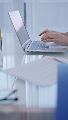 Business woman is working with laptop computer while sitting at the glass table in home office, closeup of hands