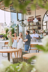 Wall Mural - Happy young people, men and women in elegant clothes having relaxing time at bar, drinking cocktails, talking, dancing. Concept of friendship, party, leisure, celebration, relaxation