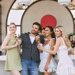 Wall Mural - Group of friends, men and women sharing joyful moment at stylish bar, enjoying refreshing cocktails and good company. Concept of friendship, party, leisure, celebration, relaxation