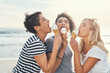 © A. Frank/peopleimages.com - Friends, women and eating with ice cream outdoor for fun bonding, hungry and sugar dessert in summer together. Group, people and relax with gelato snack, enjoy and food for joyful memory on beach