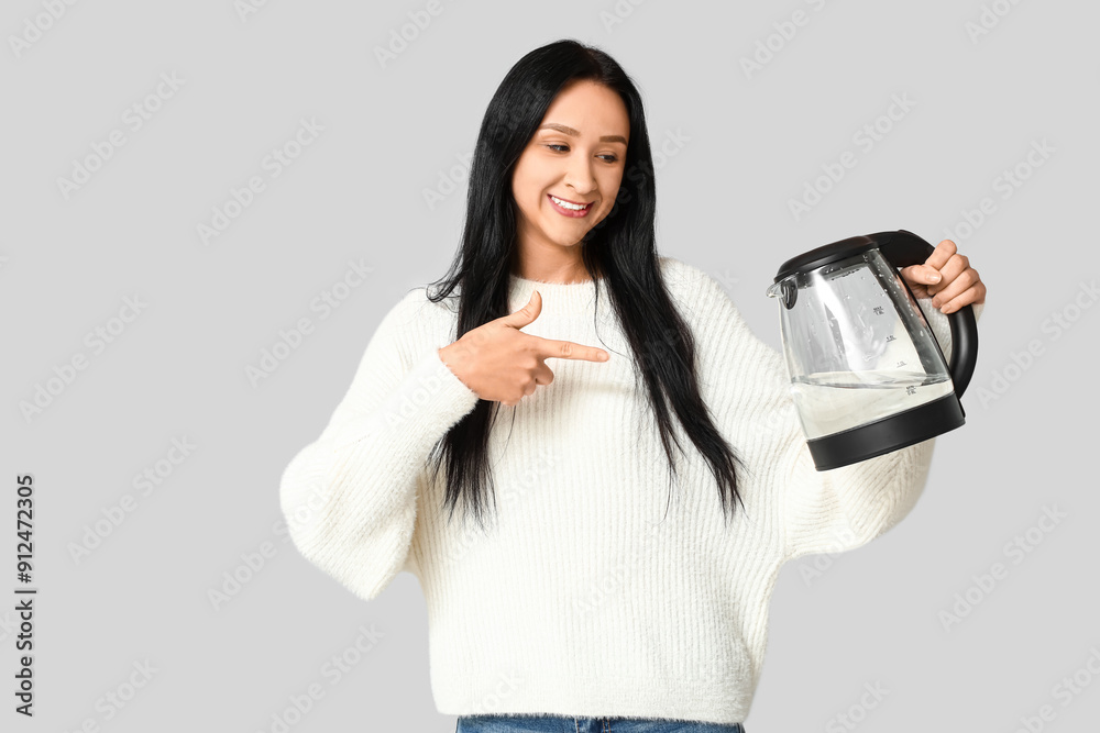 Beautiful young woman pointing at modern electric kettle on grey background