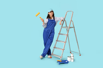 Wall Mural - female asian painter with rollers, paint cans, tray and stepladder on blue background