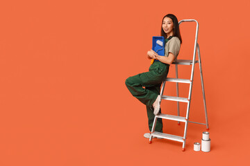 Wall Mural - female asian painter with roller, tray, paint cans and stepladder on orange background