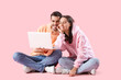 © Pixel-Shot - Happy young couple with laptop on pink background