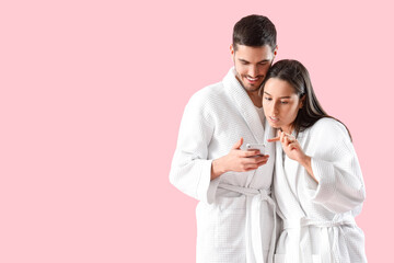 Poster - Happy young couple in robes with mobile phone on pink background