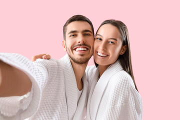 Canvas Print - Happy young couple in robes taking selfie on pink background