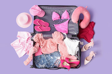 Open suitcase with belongings on lilac background. Travel concept