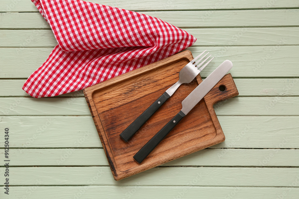 Table setting with board, cutlery and napkin on green wooden background