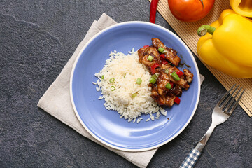 Wall Mural - Tasty sweet and sour chicken with rice in plate, vegetables and fork on black grunge background