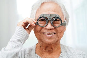 Wall Mural - Asian senior woman wearing ophthalmic vision eye test and using optical trial frame.