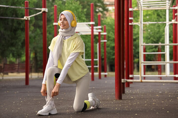 Poster - Sporty Muslim woman in headphones tying shoelaces outdoors