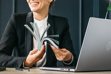 Businesswoman in a modern office with a laptop, enjoying a large sum of money. Perfect for showcasing financial success and confidence in business. Highlight your achievement and self-assurance