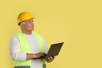 Wall Mural - Engineer in hard hat with laptop on yellow background, space for text