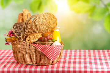 Poster - Picnic basket with foods and juice on table in nature. Space for text