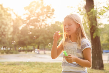 Sticker - Cute happy little girl blowing soap bubbles in park