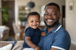 © GraysonStock - A middle-aged African-American father holding his baby in his arms, smiling showing love to his child.