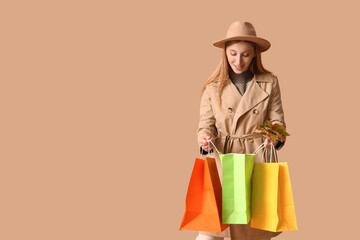 Poster - Young woman in autumn clothes with shopping bags and leaves on brown background