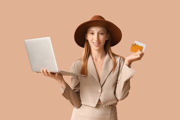 Poster - Young woman in autumn clothes with laptop and credit cards on brown background. Online shopping