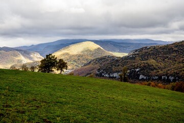 Sticker - Scenic view of rolling hills under a cloudy sky with patches of sunlight illuminating the landscape