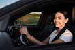 © New Africa - Smiling young woman holding steering wheel while driving car, view from outside