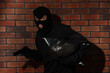 © New Africa - Thief in balaclava with gun and bag against red brick wall