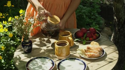 Wall Mural - Woman pouring tea into ceramic mug on wooden garden table.