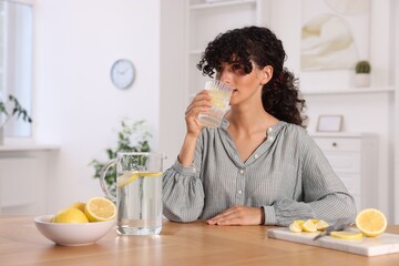 Wall Mural - Woman drinking water with lemon at table indoors