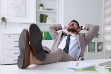 Wall Mural - Smiling businessman with hands behind his head holding legs on table in office. Break time