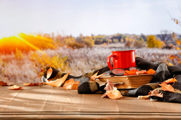 Poster - Red mug and black tablecloth on wooden table. Autumn still life on wooden table. Autumn sunlight and field background.