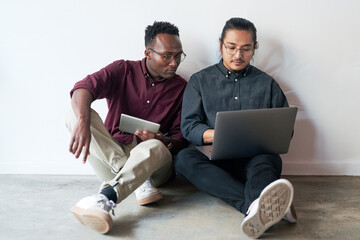 Canvas Print - Teamwork, laptop and tablet of business people on floor, planning and research for startup in office. Career, men or web developer with technology for layout design, solution and creative agency