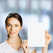 © vgstudio - Portrait of cheerful smiling woman wear white cloth, holding showing demonstrate mock up paper signboard, indoors. Business advertising ad concept. Empty free area for ad text. Square image.