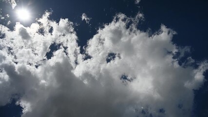 Wall Mural - time lapse looking up at a dark blue summer sky as clouds pass in front of a bright sun. the sun cre
