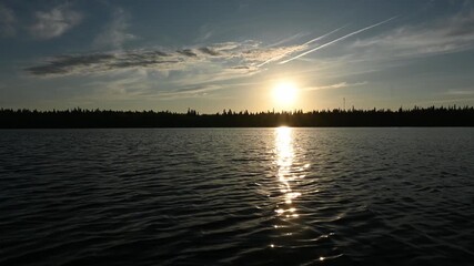 Wall Mural - Paddling a canoe across a large lake as the sun is setting above a northern forest. The canoeist’s paddle and hands can be seen moving as they paddle the boat.
