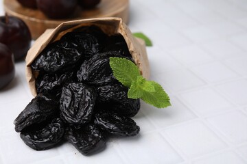 Wall Mural - Paper bag with tasty dried plums (prunes) and mint on white tiled table, closeup. Space for text