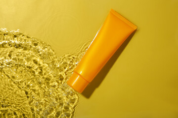 Wall Mural - Tube with cream in water on yellow background, top view. Cosmetic product