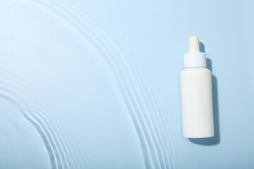 Wall Mural - Bottle of cosmetic product in water on light blue background, top view. Space for text