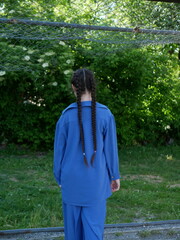 A girl with two pigtails in blue clothes standing on a green natural background