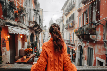 Poster - Brunette woman in autumn warm orange cardigan against the background of the city. Back view