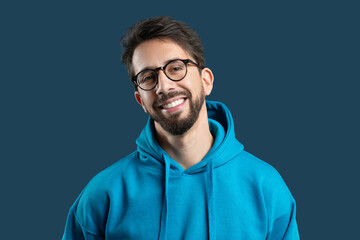 Man exudes a cheerful demeanor, showcasing a bright smile. He is dressed in a vibrant blue hoodie, adding a pop of color to the simple yet captivating backdrop.