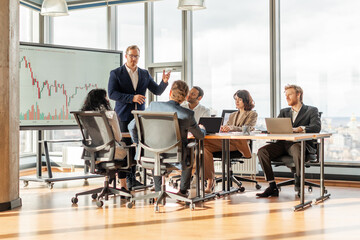 Aufkleber - A group of business professionals are gathered around a conference table in a modern office. A presenter stands in front of the group, pointing to a large screen displaying a financial chart