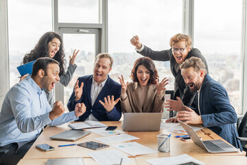 Aufkleber - A team of five business professionals, dressed in suits and business casual attire, gather around a conference table in an office setting. They are all excitedly celebrating a success