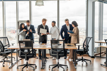 Aufkleber - A diverse group of business professionals stand around a conference table in a modern office space. They are engaged in a lively discussion