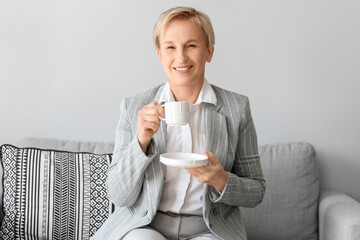 Poster - Mature businesswoman drinking coffee while sitting on sofa in office